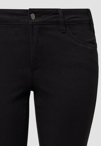 Čierne denimové nohavice s priliehavým strihom, s predným zapínaním na gombík, pútkami na opasok a hladkým povrchom. Detailné šitie a dizajn vreciek.