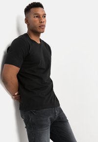 Sort bomulds t-shirt med rund hals og korte ærmer, parret med mørkegrå denim jeans. Glat tekstur, enkelt design og afslappet pasform.