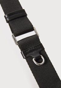 Sort nylonrem med tekstureret overflade, glatte læderdetaljer, metalhardware med D-ring og en justerbar spænde.