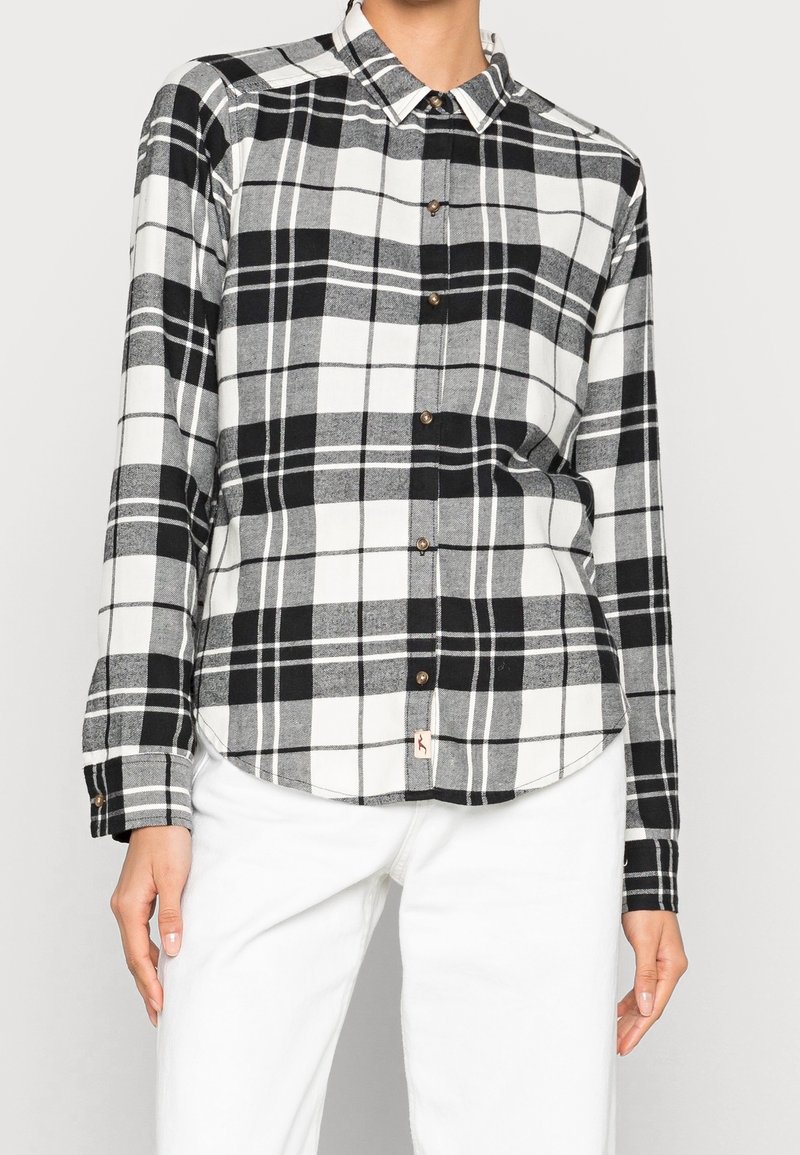 Chemise à carreaux noir et blanc à manches longues, design à boutons, ourlet arrondi et une petite étiquette logo en bas. Matériau en coton.
