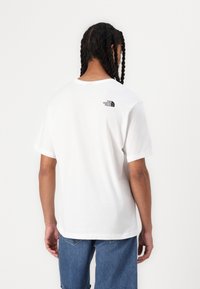 Bílý bavlněný tričko s kulatým výstřihem a krátkým rukávem. Na zadní straně se nachází černé logo v levém horním rohu.