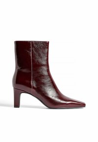 Bottine en cuir bourgogne avec un bout pointu, texture lisse et un talon bloc de hauteur moyenne. Design épuré avec un minimum de coutures.