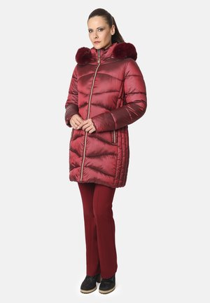 Abrigo acolchado rojo con un acabado brillante, que presenta un cierre con cremallera en la parte delantera, bolsillos laterales y un ribete de piel sintética desmontable en la capucha. Combinado con pantalones a juego.