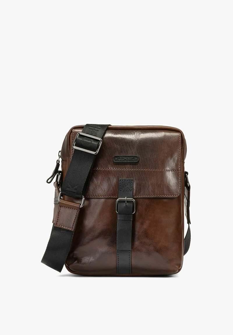 Brązowa skórzana torba na ramię o gładkiej fakturze, z czarnym regulowanym paskiem, zapięciem na klamrę z przodu oraz wytłoczonym detalem logo.