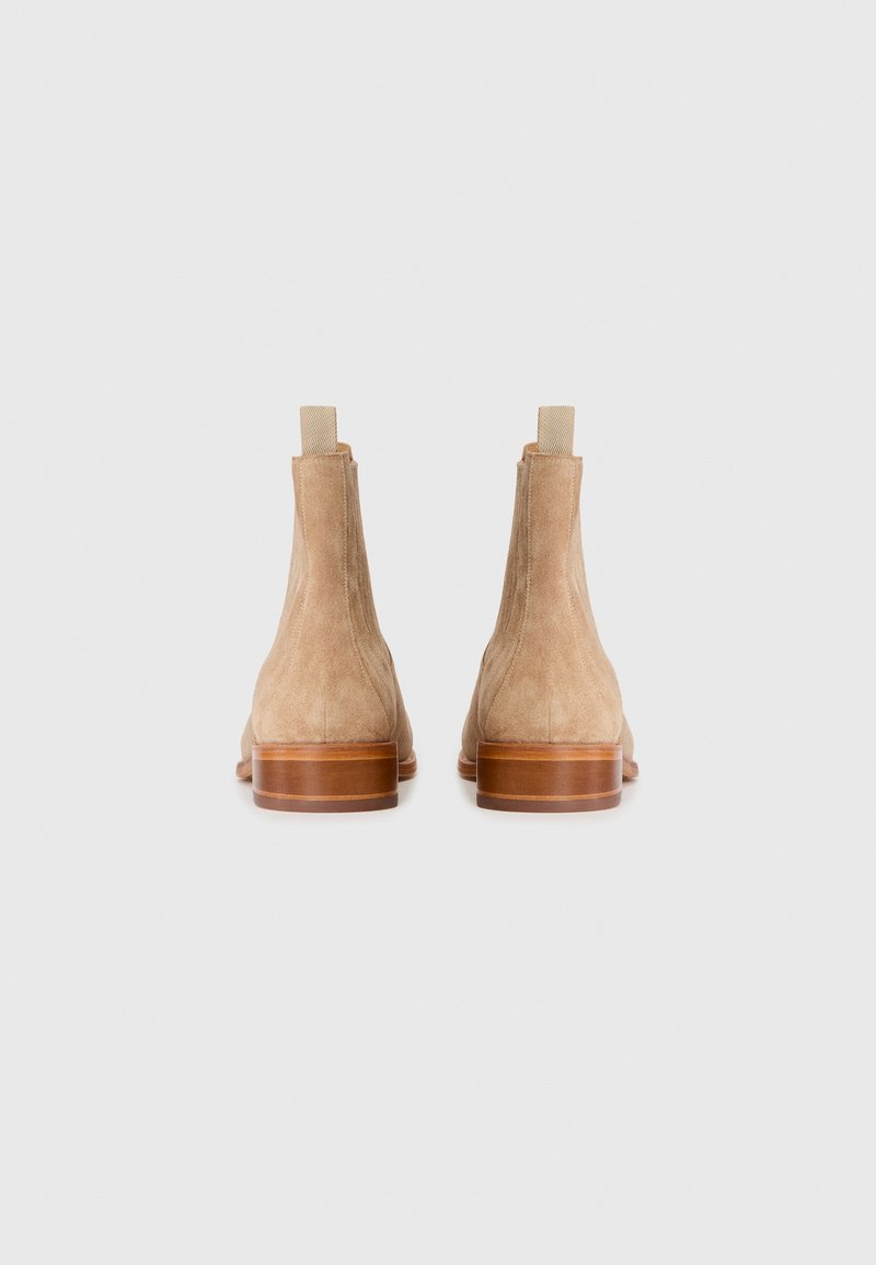 Bottines en suède beige avec un talon en bois empilé et une languette en tissu à l'arrière. Texture lisse et design minimaliste.