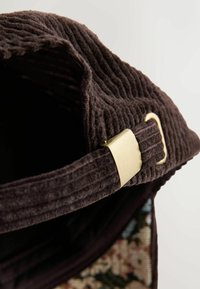 Brun kordfløjls taske med en tekstureret overflade, der har et hardware-tilbehør i guldfarve på remmen. Indvendigt er der et blomstermønster.