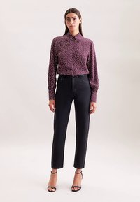 Bordeauxrood overhemd met witte polkadots, lange mouwen en een kraag, gecombineerd met zwarte, hoog taille jeans en zwarte sandalen met hak.