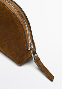 Borsa in suede marrone con forma arrotondata, zip in argento e un cinturino in tessuto per il polso. Presenta una superficie liscia e dettagli di cucitura a contrasto.