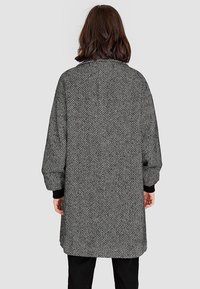 Zwart-witte visgraat ontworpen jas met oversized mouwen, een ontspannen pasvorm en effen zwarte boorden, die een gestructureerde stof toont.