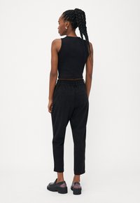 Black cropped tank top, high-waisted black pants with elastic waistband, and chunky black shoes with a slight purple gradient. Rear view shown.