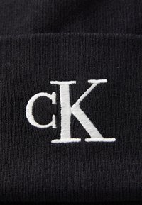 Beanie nero a maglia con texture a coste, dotato del logo "cK" ricamato in bianco, ben visibile sulla parte anteriore.