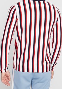 Langärmeliges Hemd mit horizontalen Streifen in Rot, Marineblau und Weiß. Weicher Baumwollstoff mit rundem Ausschnitt und tailliertem Design.