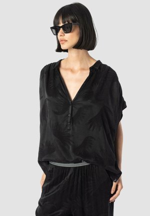Black short-sleeve blouse with a V-neck, featuring a subtle hand print pattern. Made from soft fabric, paired with textured black trousers.