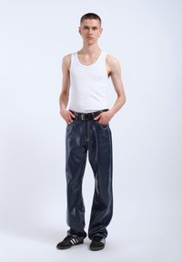 White tank top, blue synthetic pants with a shiny texture and visible stitching. Black belt and black sneakers with white stripes.