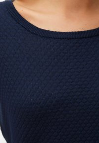 Maglione lavorato a maglia di un blu navy con un motivo a rombi testurizzato e un ampio scollo a giro. La vista ravvicinata mette in evidenza la trama del tessuto.