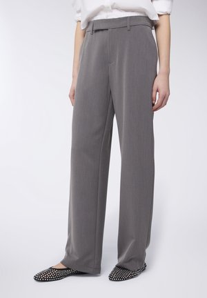 Pantaloni grigi su misura con design a gamba dritta, caratterizzati da una parte frontale piatta, passanti per la cintura e una sottile trama. Ballerine nere con borchie completano l'outfit.