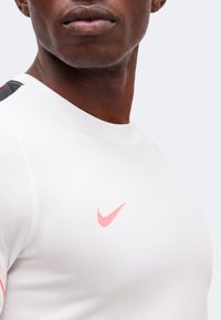 Close-up of a person wearing a white Nike shirt with a pink logo, showing the neck, lower face, and upper chest area.