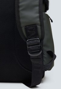 Plecak z czarną siatkowymi korpusem i zielonymi syntetycznymi akcentami, wyposażony w szeroki pasek z plastikowym zapięciem i teksturowanym detalem z materiału.