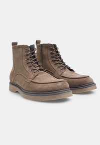 Botine din suedă maro, până la gleznă, cu un design cu șireturi, având vârful rotund, detalii cusute și talpă din cauciuc pentru aderență.