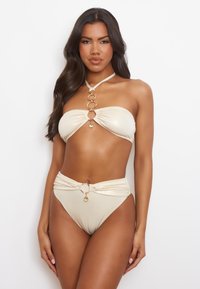 Bikini-set van lichtbeige stof met een bandeau-top voorzien van decoratieve gouden ringen en een hoogwonder-bottom met een accentdetail.