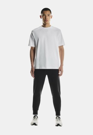 Hvid bomulds T-shirt med korte ærmer, parret med sorte tapered sweatpants. Model bærer hvide og sorte sportssko.