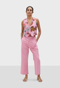 Růžový květinový crop top s výstřihem do V a dekoračními detaily, zkombinovaný s volnými růžovými kalhotami a sandály na řemínky.
