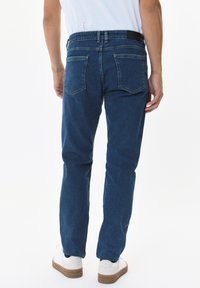Modre denim hlače z ravnim krojem, ki vključujejo klasičen pet-pocket dizajn in črn poudarjen pas. Oblečene z belimi supergami.