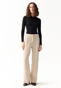 Czarny bodysuit z długim rękawem w połączeniu z kremowymi spodniami o szerokich nogawkach w pionowe paski, uszytymi z teksturowanej tkaniny. Czarne obuwie.