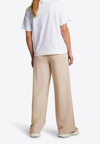 Camiseta blanca de algodón de manga corta, combinada con pantalones beige de pierna ancha, que presentan una textura suave y un corte relajado. Sin patrones visibles.