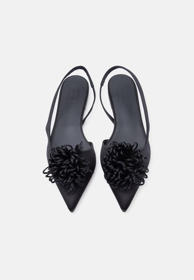 Μαύρα μυτερά παπούτσια με λουράκι και διακοσμητικά με λουλούδια σε μορφή θηλιάς στα δάχτυλα, απεικονισμένα από πάνω σε λευκό φόντο.