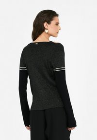 Maglione nero lavorato a maglia con fili metallici, maniche lunghe nere e strisce bianche vicino alle spalle; presenta un dettaglio con logo sulla parte posteriore del colletto.