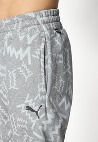 Nærbillede af grå Puma sweatpants med hvide abstrakte zigzag-mønstre og et sort Puma-logo nær lommen.