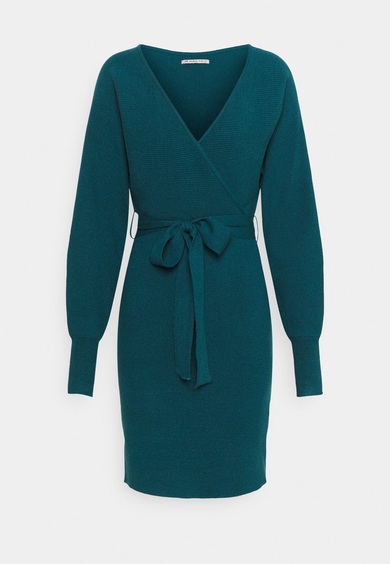 Robe portefeuille en maille bleu sarcelle avec manches longues, encolure en V profonde, poignets ajustés et nœud à la taille, sur fond uni.