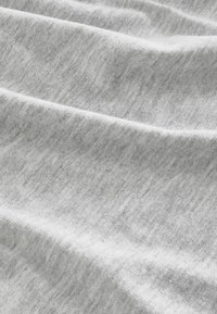 Tessuto grigio chiaro che mostra una texture morbida e liscia con pieghe delicate, che indicano un materiale leggero, possibilmente cotone o una miscela di cotone.