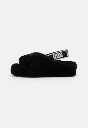 Sort fluffy åben-tå hjemmesko med tyk sål og sort elastisk hælrem med hvid UGG-logo tekst.