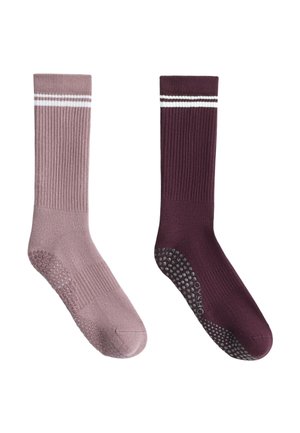 Une paire de chaussettes antidérapantes rose poussiéreuse et une violette foncée avec des rayures blanches près du haut, présentées côte à côte sur un fond blanc.