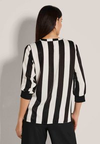 Zwart-wit gestreept T-shirt met driekwartmouwen, ronde hals en zachte textuur, gezien vanaf de achterkant.