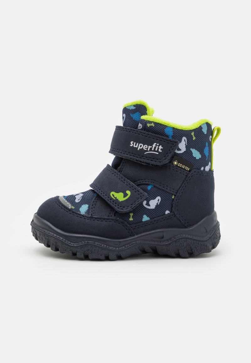 Bottes pour enfants de la marine avec des accents verts, dotées de bandes Velcro, d'une semelle texturée et d'un dessus en tissu à motifs avec des designs colorés.