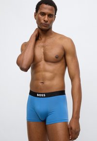 Blauwe boxershorts met een zwarte tailleband met het label "BOSS." Gladde stof, nauwsluitend ontwerp, tot halverwege de dij en met een lichte glans.