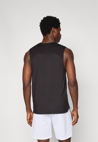 Svart ermeløs treningstopp med rund hals, jevn tekstur og minimal sømdetaljer, kombinert med lyse shorts.