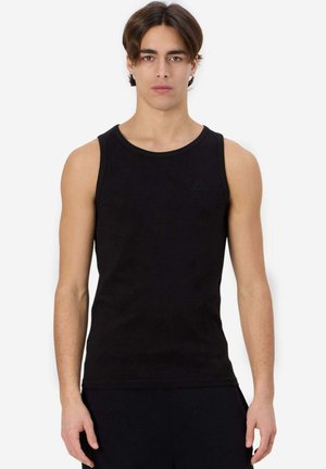 Giovane uomo con capelli castano medi, indossa una canotta nera aderente senza maniche, in piedi davanti a uno sfondo bianco.