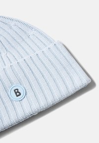 Jasnoniebieska czapka typu beanie z prążkowanego dzianiny, z podwiniętym mankietem i okrągłą naszywką z czarną literą "B" na dopasowanym niebieskim tle.