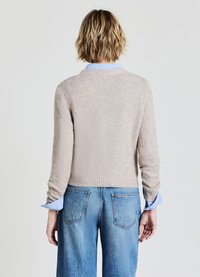 Beige gestrickter Pullover mit strukturiertem Finish und geripptem Saum, kombiniert mit hellblauen Jeans aus Denim, die seitliche Taschen und einen lockeren Schnitt haben.