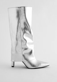 Botte montée en simili cuir argenté avec un bout pointu, un design épuré et un petit talon carré ; présente une texture lisse et réfléchissante.