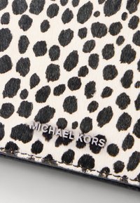 Materijal s uzorkom crnih i smeđih leoparda s glatkim, teksturiranim osjećajem. Sadrži srebrni logo "MICHAEL KORS" na svijetloj pozadini.