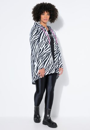 Kapuzensweatshirt mit Zebramuster in Schwarz und Weiß mit pinken Akzenten, kombiniert mit glänzenden schwarzen Leggings und schwarzen Stiefeletten. Weicher, entspannter Schnitt.