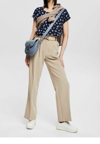 Granatowa bluzka w kwiaty; beżowe spodnie z wysokim stanem; jasnobrązowy sweter przewieszony przez ramiona; niebieska torba na ramię; białe sneakersy.