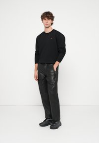 Sweatshirt preta com um pequeno logótipo, combinada com calças cargo pretas brilhantes com bolsos com fecho éclair e ténis pretos texturizados.