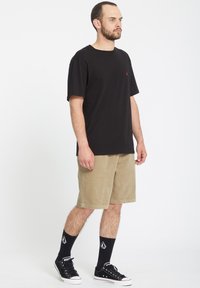 Sort bomulds T-shirt, løs pasform, parret med beige fløjlsshorts. Båret med sorte sokker og sorte sneakers med hvide såler.