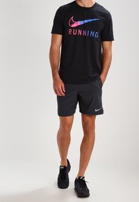 Černé tričko Nike s barevným potiskem "RUNNING", v kombinaci s černými šortkami a černými sportovními botami. Jednoduchý design, pohodlný střih.